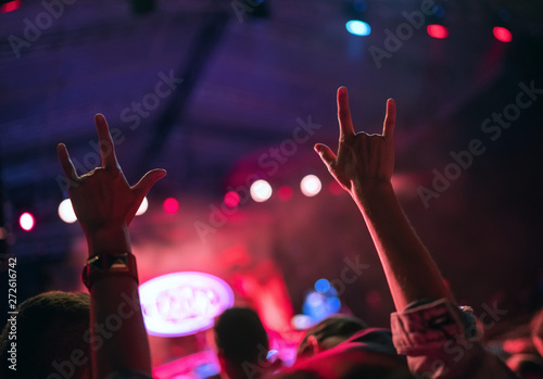 Young teenager girl raised up two hands with sign of the horns gesture supporting favorite rock band on the night concert