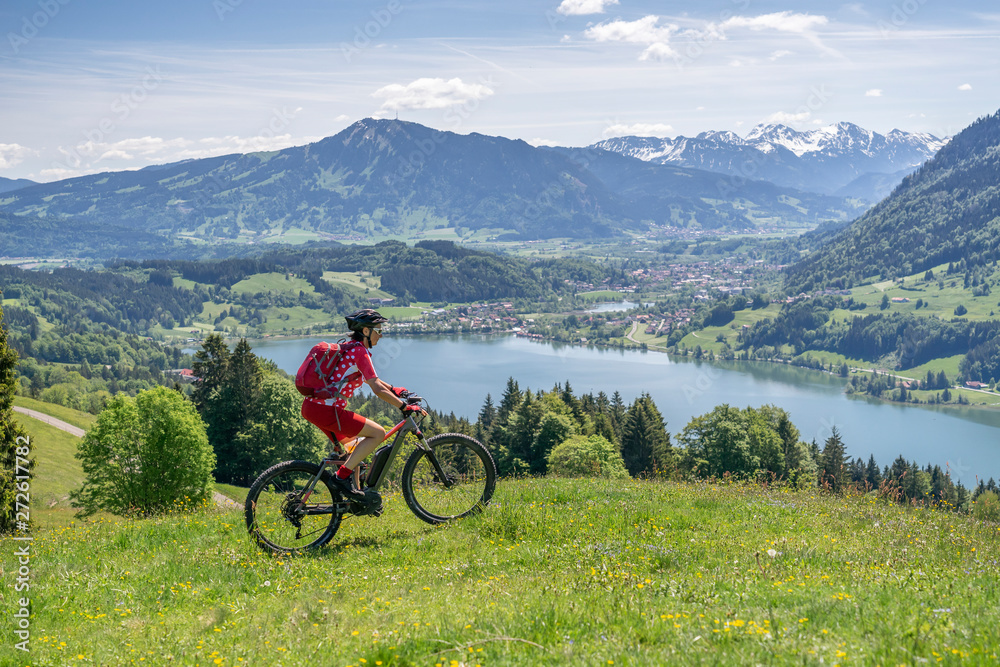 Fototapeta premium senior woman riding her electric mountain bike in springtimeon the mountains above the Alpsee near Immenstadt, Allgau,Bavaria, Germany