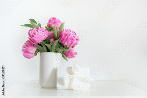Bouquet of pink peony in vase with gift on white. Copy space for text. Mothers day.
