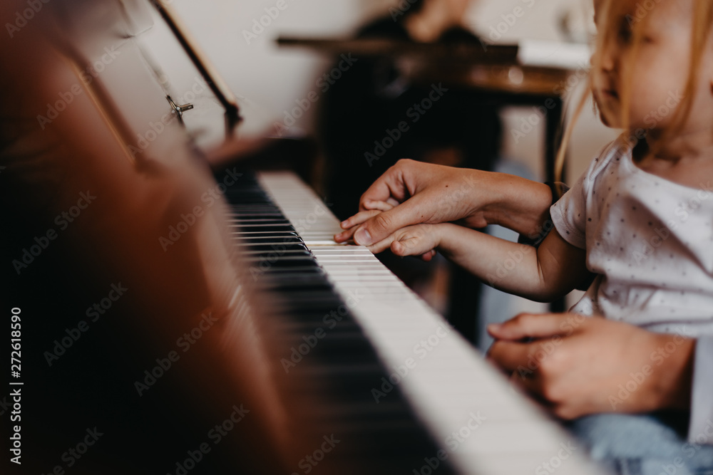 Obraz premium Cute little happy child girl playing piano in a light room. Selective focus, noise effect