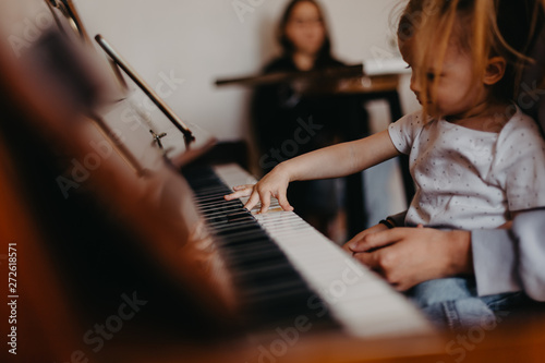 Mother teaches a little girl to play the piano. They play and sing songs. Its fun, Cute happy child girl playing piano in a light room. Selective focus, noise effect