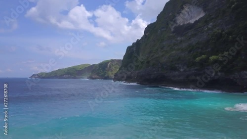 Aerial footage from drone - ocean coastline, small people and rock on background, blue waves.