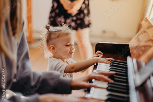 Cute little happy child girl playing piano in a light room Fototapete