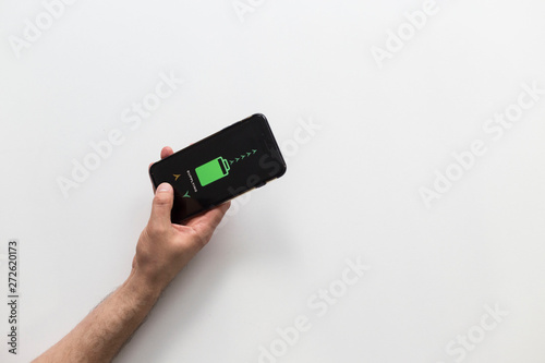 Hand holding black smart phone while it’s wireless charging on white background.