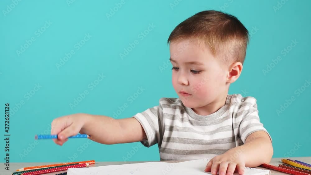 Inspired little boy at the table draw with pencils, isolated on blue Inspired little boy at the table draw with pencils, isolated on blue