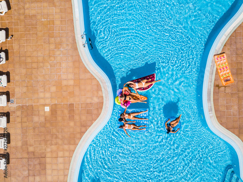 Top high aerial view of group of female caucasian people enjoying the pool with coloured trendy lilos mattress - summer holiday vacation hotel concept with blue water and relaxed funny girls