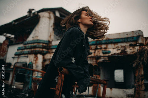 Young woman posing against the background of an old abandoned ship.