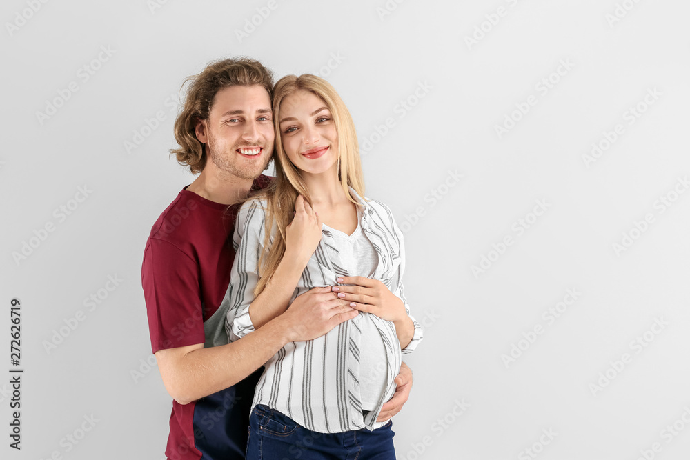 Happy young pregnant couple on light background Happy young pregnant couple on light background