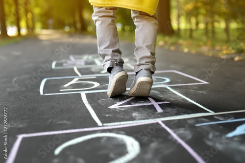 Closeup of little boy's legs and hopscotch drawn on asphalt. Child playing hopscotch game on playground outdoors on a sunny day. photo