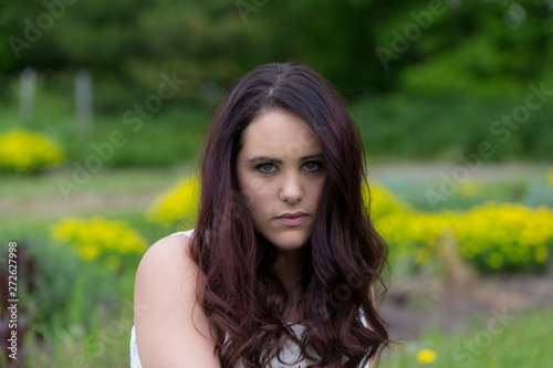 Horizontal closeup of pretty brunette young woman with serious intent expression and long wavy hair against floral soft focus background