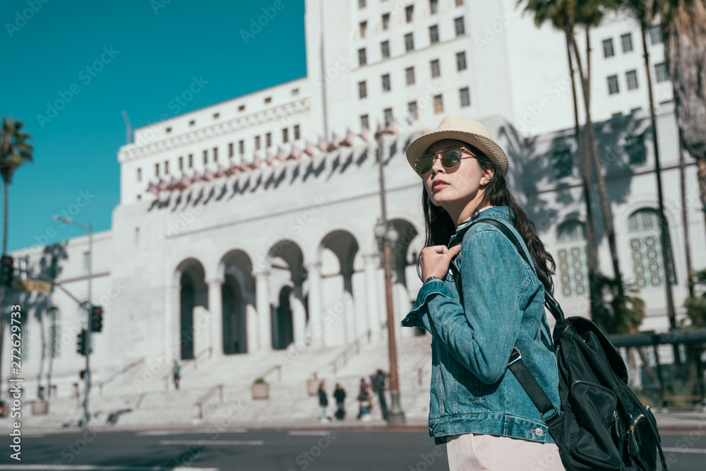 vintage style photo young stylish girl tourist in sunglasses carry bag walking in urban on street looking around sightseeing with blue sky. Los Angeles city hall on sunny day California in background
