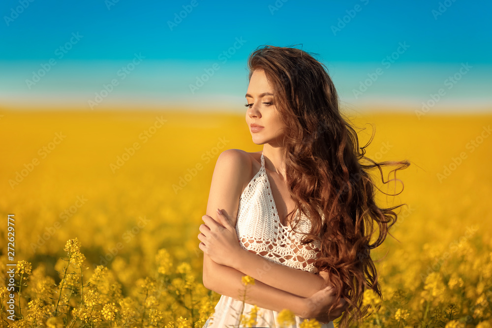 Beautiful carefree girl with long curly healthy hair over Yellow rape field landscape background. Attracive brunette with blowing hairstyle enjoying and breathing sunset, outdoor beauty portrait. Beautiful carefree girl with long curly healthy hair over Yellow rape field landscape background. Attracive brunette with blowing hairstyle enjoying and breathing sunset, outdoor beauty portrait.