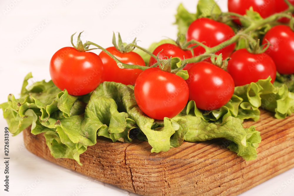 Ripe fresh Juicy organic brunch of cherry tomatoes on cutting board with Green Lettuce on a white table