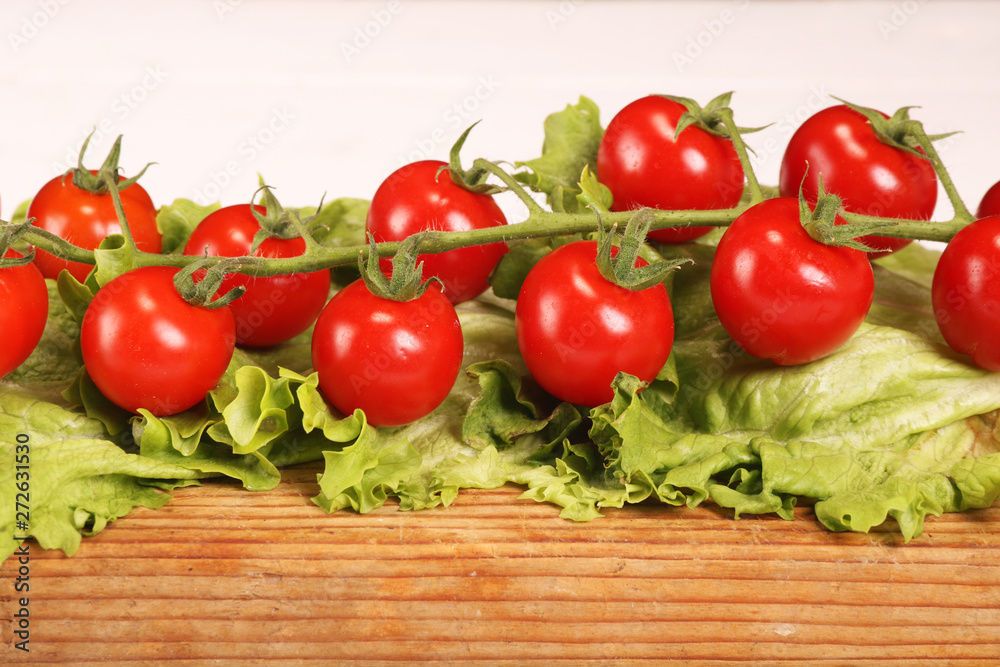 Ripe fresh Juicy organic brunch of cherry tomatoes on cutting board with Green Lettuce on a white table Ripe fresh Juicy organic brunch of cherry tomatoes on cutting board with Green Lettuce on a white table