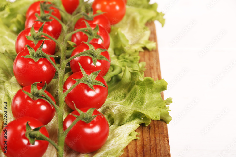 Ripe fresh Juicy organic brunch of cherry tomatoes on cutting board with Green Lettuce on a white table Ripe fresh Juicy organic brunch of cherry tomatoes on cutting board with Green Lettuce on a white table