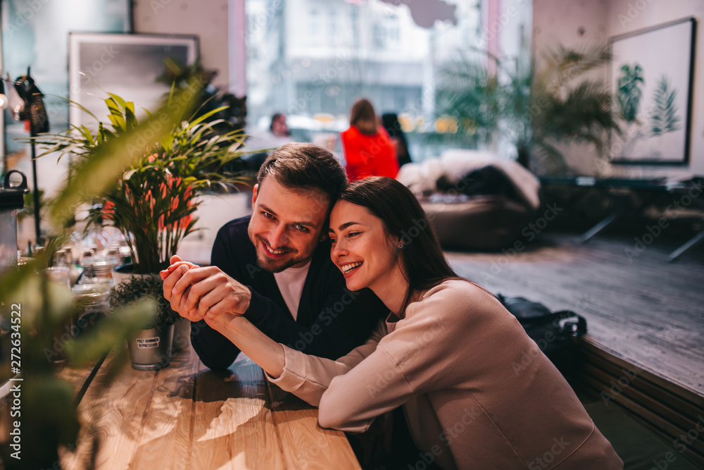 Fototapeta premium Happy loving guy holds his girlfriend's hand sitting at the table in the cafe and looks at her.
