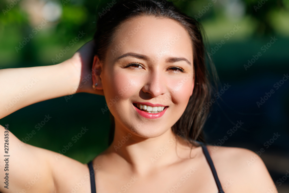 close up portrait of a young beautiful smiling happy brunette girl in outdoor Park on a Sunny summer day correcting hand loose hair close up portrait of a young beautiful smiling happy brunette girl in outdoor Park on a Sunny summer day correcting hand loose hair