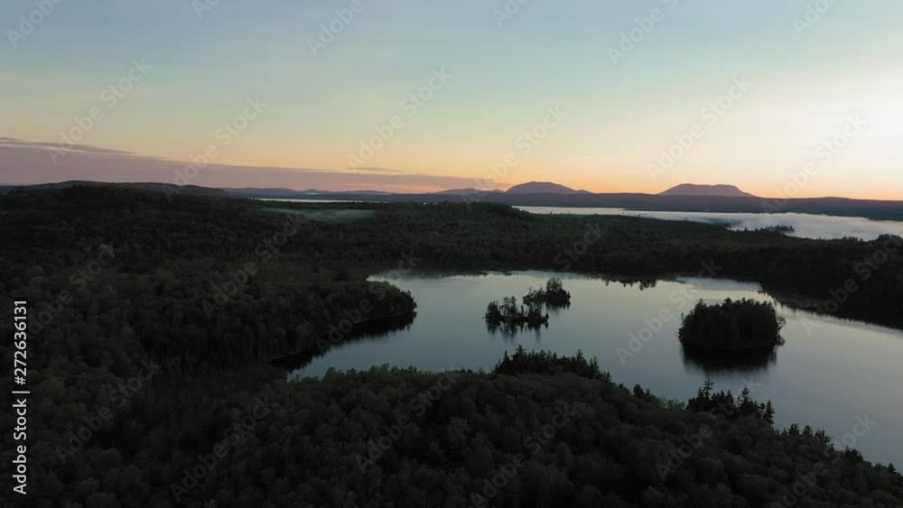 Flying over a calm pond at sunrise with backlit hills and fog in the distance AERIAL Flying over a calm pond at sunrise with backlit hills and fog in the distance AERIAL