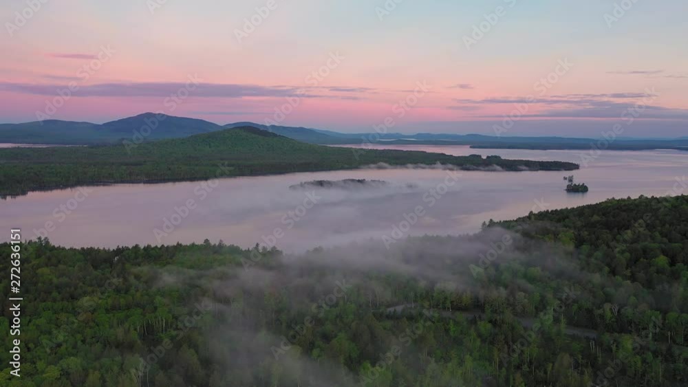 Flying high over a misty covered forest towards a calm lake in the distance