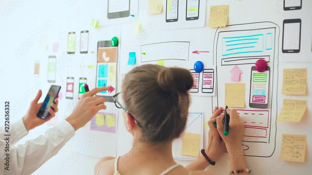 Designers is developing a web application for mobile phones. Woman draws a mockup of interface to smartphone. User experience. 