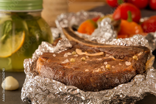 Meat steak baked in foil and baked vegetables with a steamed mug of mint drink on a wooden table. Close-up