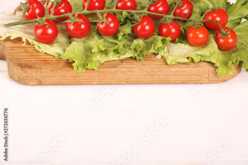 Ripe fresh Juicy organic brunch of cherry tomatoes on cutting board with Green Lettuce on a white table. Copy space