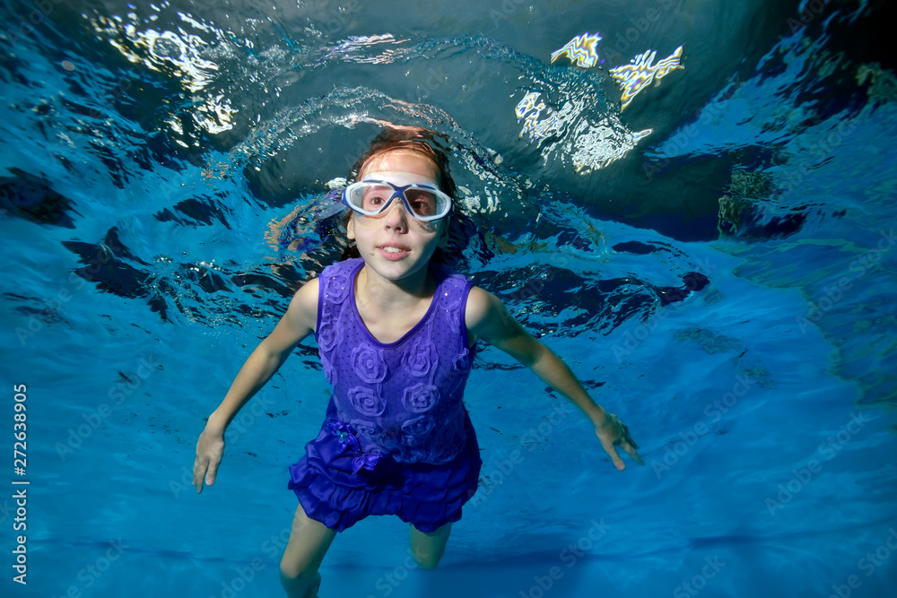Cute little girl swimming underwater in the pool. She smiles and looks ...