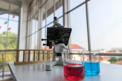 The scientific microscope for testing with the laboratory glassware on the white table.