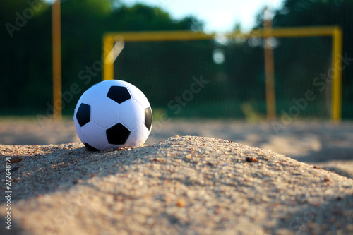 soccer ball close-up in the left part of the frame on the evening sunny beach and blurred goal in the background