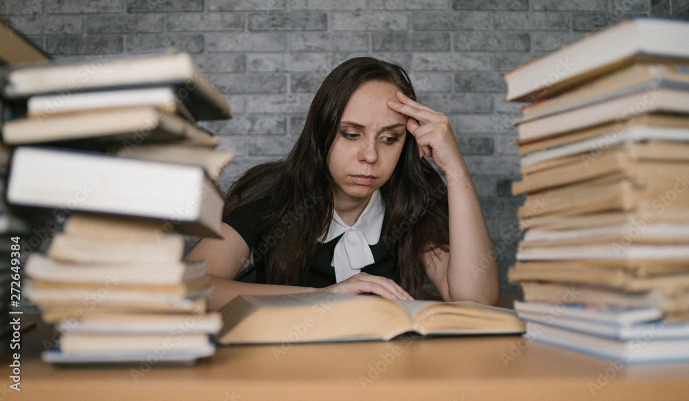 Woman student boring reading book at library with a lot of books in university. Student disheartened reading book for examination. Woman student boring reading book at library with a lot of books in university. Student disheartened reading book for examination.