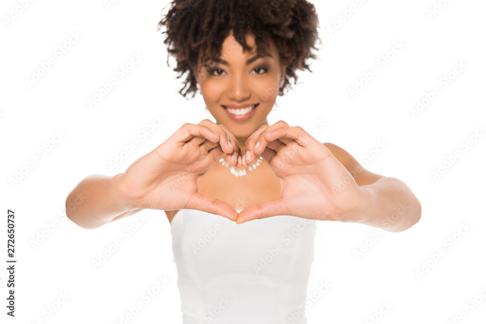 selective focus of happy and curly african american bride showing heart with hands isolated on white