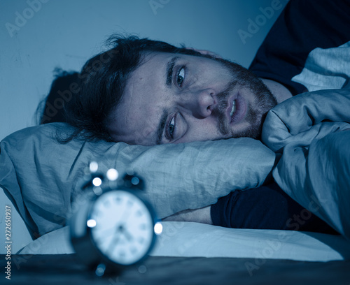 Cuadro en lienzo Young man in bed staring at alarm clock trying to sleep feeling stressed and sle