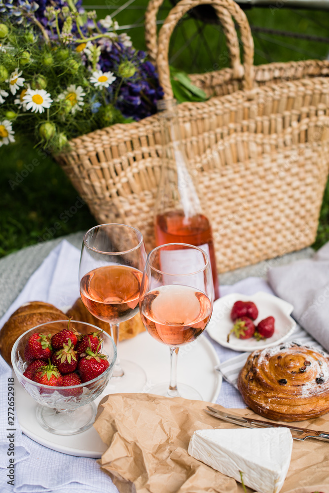 Beautiful summer picnic with strawberries, cheese and rose wine on the lawn in the city park Beautiful summer picnic with strawberries, cheese and rose wine on the lawn in the city park