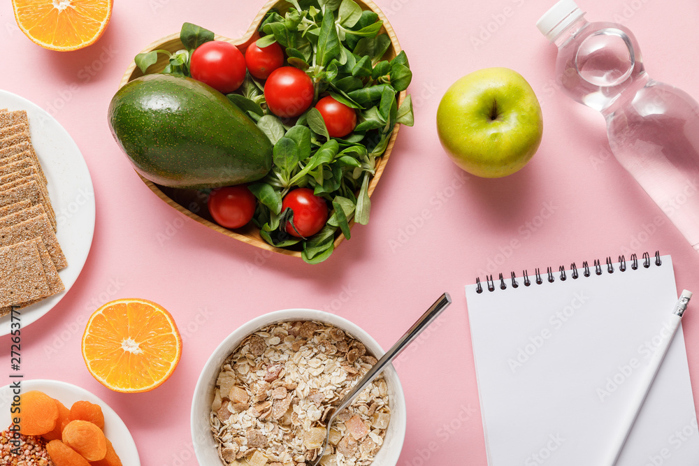 top view of fresh diet food, blank notebook with pencil and water on pink background top view of fresh diet food, blank notebook with pencil and water on pink background