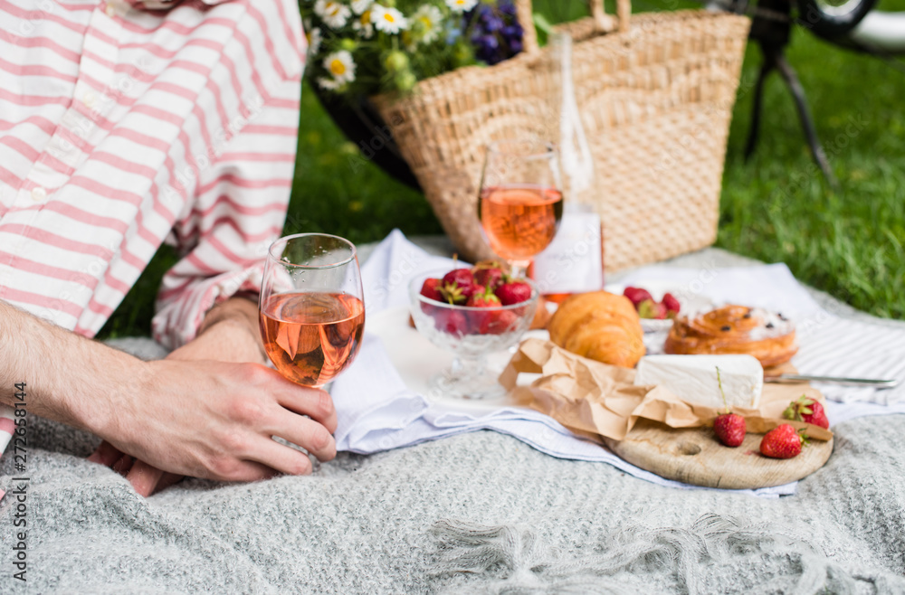 Man's hand holding glass of rose wine, summer picnic with cheese and wine