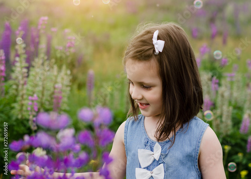 Portrait of little girl in flowers. Cute smiling kid in Blooming Lupine flowers field. Lupinus polyphyllus field