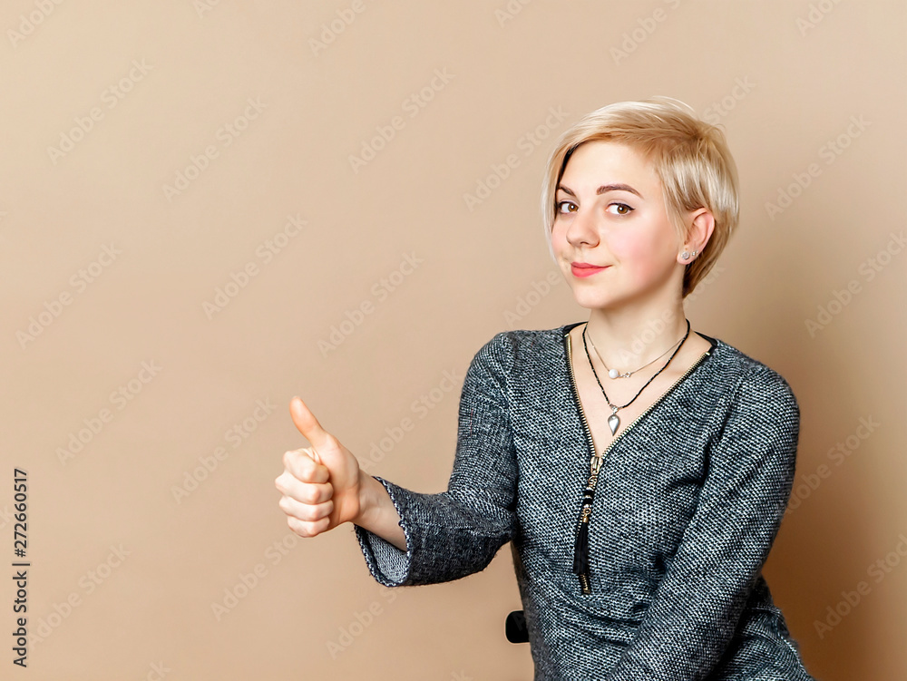 Attractive young girl with blonde short hair shownig thumbs up on cream colored background. Copyspace photo. Advertisement concept for barbershop. Attractive young girl with blonde short hair shownig thumbs up on cream colored background. Copyspace photo. Advertisement concept for barbershop.