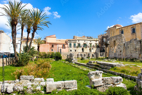 Amazing ruins of Temple of Apollo in Ortigia Island, Syracuse, Sicily, Italy. Significant ancient Greek monument, archaeological site. Temple ruins. Adjacent palm trees, sunny day, blue sky