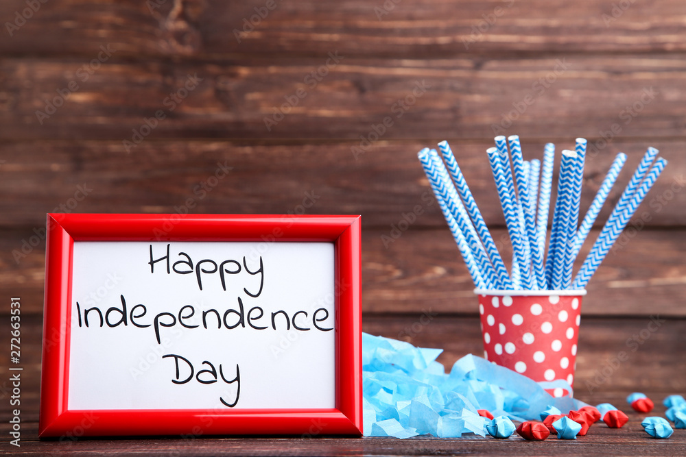 Fototapeta premium Text Happy Independence Day with paper stars and straws in cup on wooden table