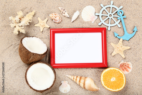 Wooden blank frame with seashells and fruits on beach sand