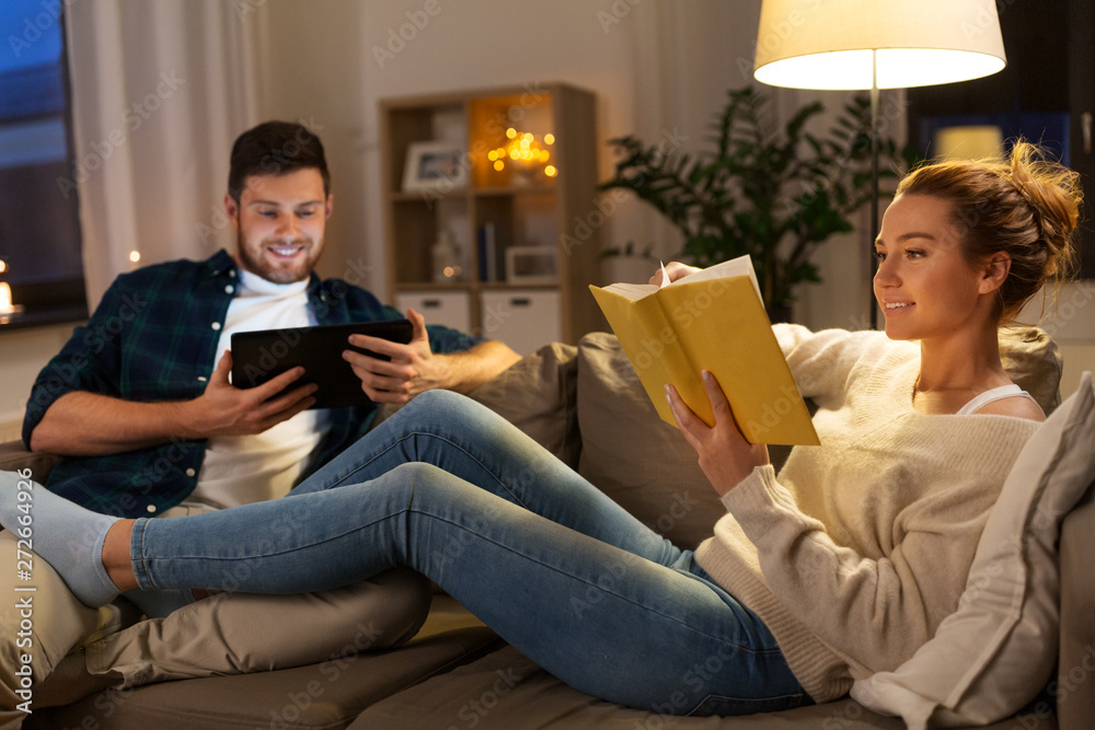 leisure and people concept - happy couple with tablet computer and book at home in evening - obrazy, fototapety, plakaty 