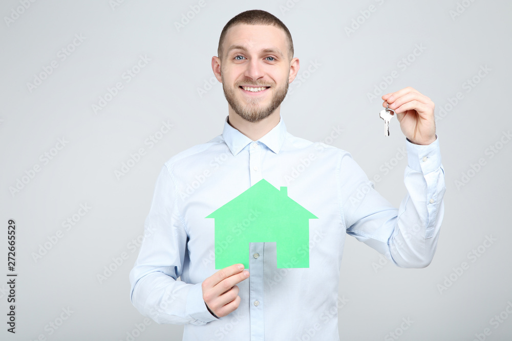 Young man with silver keys and paper house on grey background Young man with silver keys and paper house on grey background