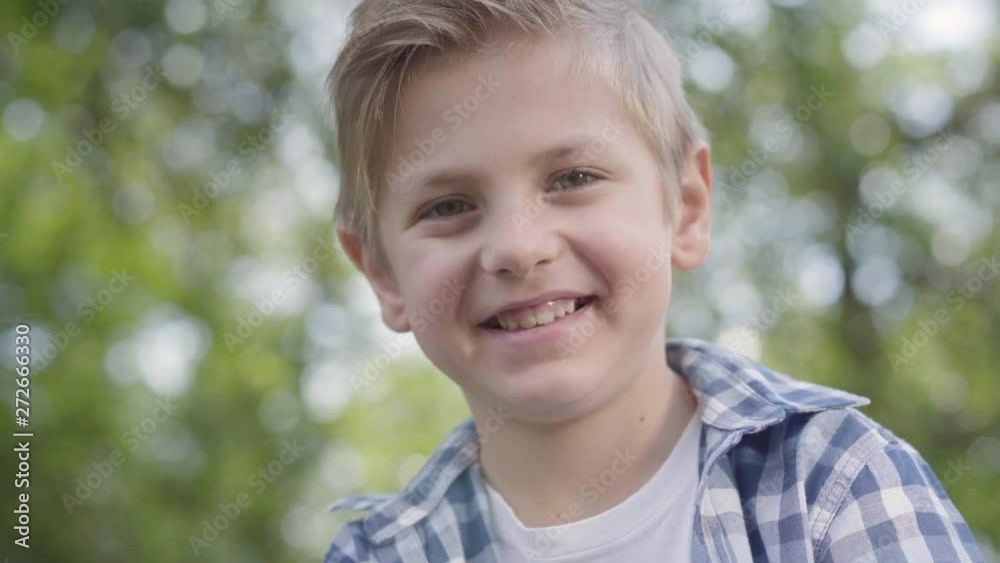 Close-up portrait of cute handsome boy in checkered shirt looking into camera sitting in the park. Summertime leisure outdoors. Lovely kid studying under the trees Close-up portrait of cute handsome boy in checkered shirt looking into camera sitting in the park. Summertime leisure outdoors. Lovely kid studying under the trees