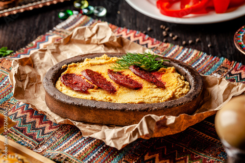 Traditional Turkish, Arabic cuisine. Hummus with salami sausage, in a clay plate, with parchment on a wood table. Serving dishes in the restaurant. copy space