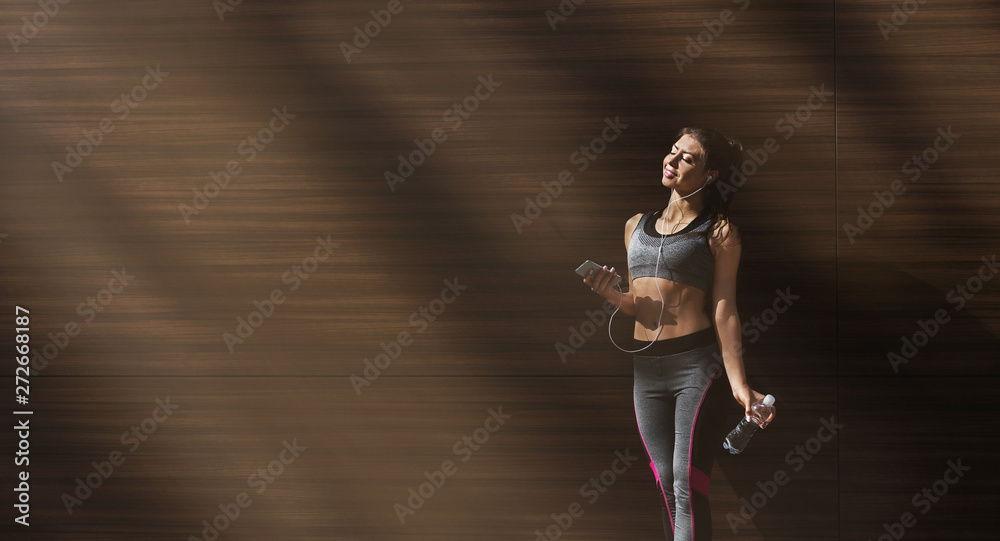 Sporty girl enjoying music in her phone on wooden background