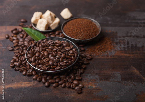 Fresh raw organic coffee beans with ground powder and cane sugar cubes with coffee trea leaf on wooden background.