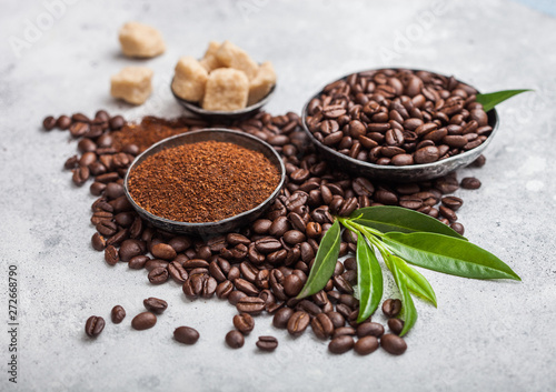 Fresh raw organic coffee beans with ground powder and cane sugar cubes with coffee trea leaf on light kitchen table background.