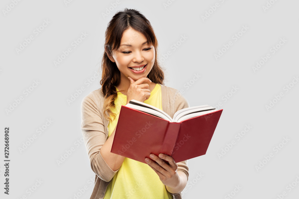 people, ethnicity and portrait concept - happy asian young woman reading book over grey background people, ethnicity and portrait concept - happy asian young woman reading book over grey background