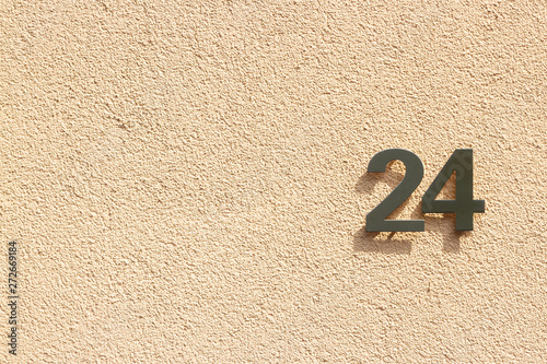 House number 24 with the twenty-four in silver with a shadow on a light orange outside wall photo