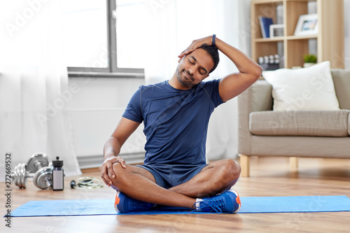 sport, fitness and healthy lifestyle concept - indian man training and stretching body at home photo